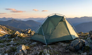 Professional 1 person backpacking tent pitched on a rocky alpine ridge at sunset, demonstrating wind-resistant pole geometry and specialized outdoor gear performance.