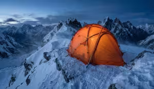 An orange geodesic 4 season backpacking tent pitched on a snowy mountain ridge, demonstrating high snow load capacity and thermal insulation during a winter storm.